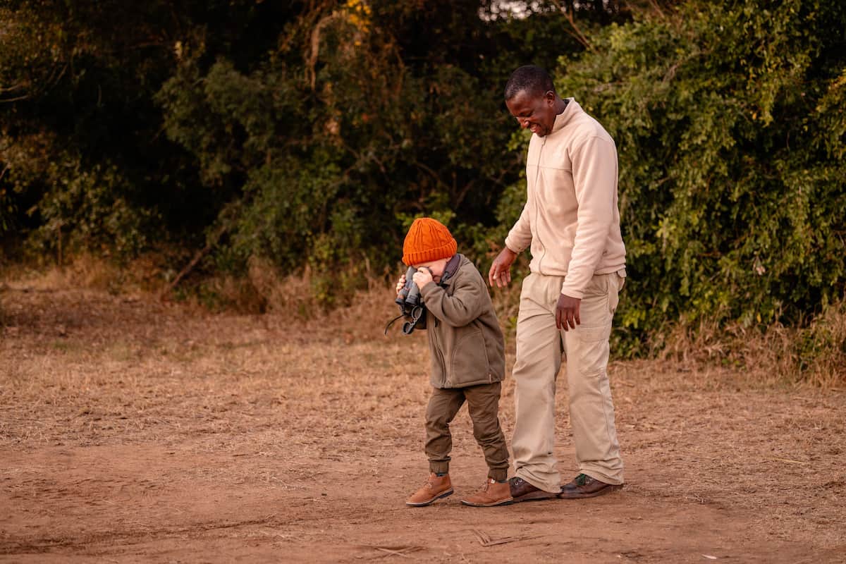 homem observa criança com binóculos observando o solo e mata nativa ao fundo